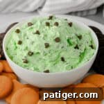 Bowl of mint chocolate chip dip topped with chocolate chips, surrounded by vanilla wafers and chocolate sandwich cookies.