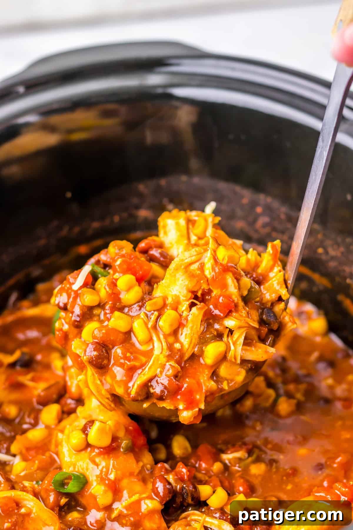 A ladle lifting a serving of easy slow cooker chicken taco soup with shredded chicken, corn, black beans, and diced tomatoess from a crockpot.