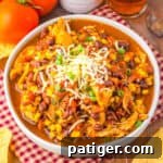 A bowl of chicken taco soup recipe topped with shredded cheese and green onions, surrounded by tortilla chips.