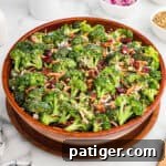 A large wooden bowl filled with broccoli crunch salad, made with fresh broccoli, bacon bits, dried cranberries, shredded carrots, sunflower seeds, and chopped red onions, all lightly coated in a creamy dressing.