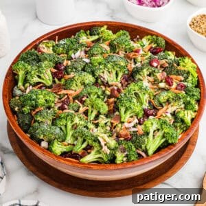 A large wooden bowl filled with broccoli crunch salad, made with fresh broccoli, bacon bits, dried cranberries, shredded carrots, sunflower seeds, and chopped red onions, all lightly coated in a creamy dressing.