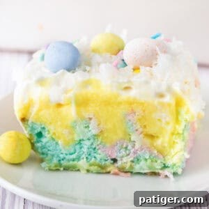 A slice of pastel Easter poke cake topped with whipped cream, coconut, and mini chocolate eggs.