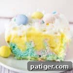 A slice of pastel Easter poke cake topped with whipped cream, coconut, and mini chocolate eggs.