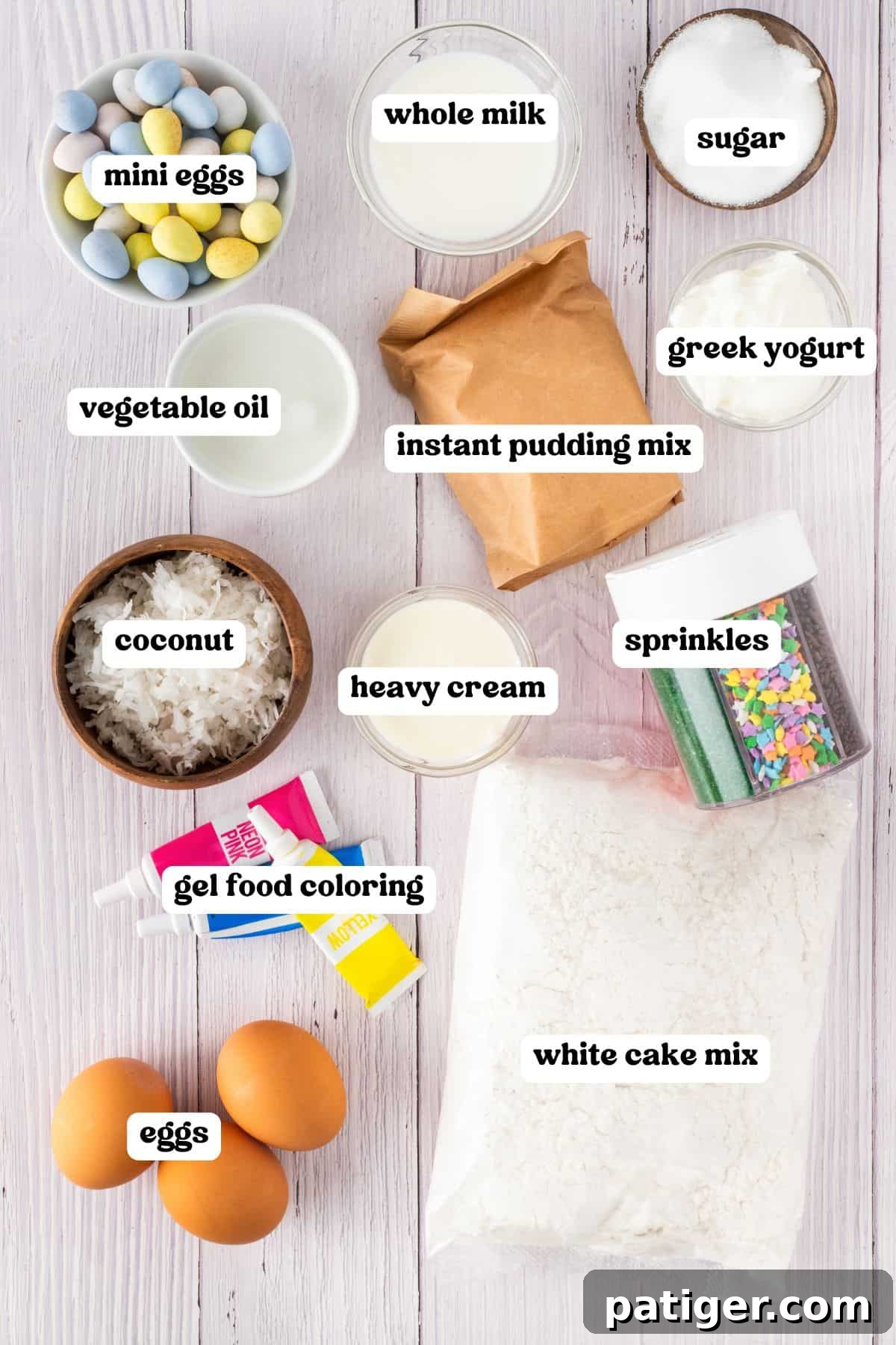 Ingredients for an Easter poke cake, each labeled. Items include white cake mix, eggs, whole milk, sugar, Greek yogurt, instant pudding mix, heavy cream, vegetable oil, shredded coconut, sprinkles, pink, blue, and yellow gel food coloring, and mini chocolate eggs.