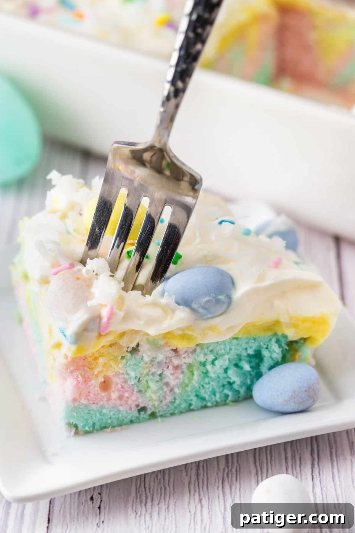 A fork digging into a slice of pastel Easter poke cake.