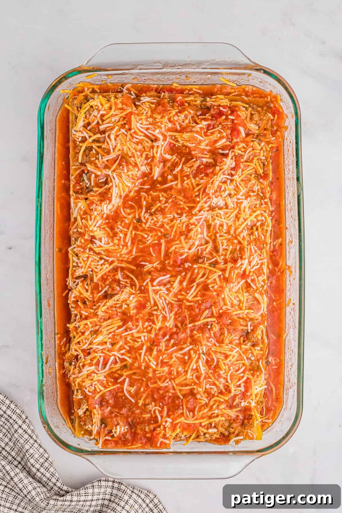A glass 9x13 baking dish brimming with pre-baked layered taco lasagna, richly covered with a vibrant red salsa topping, ready for its oven journey.