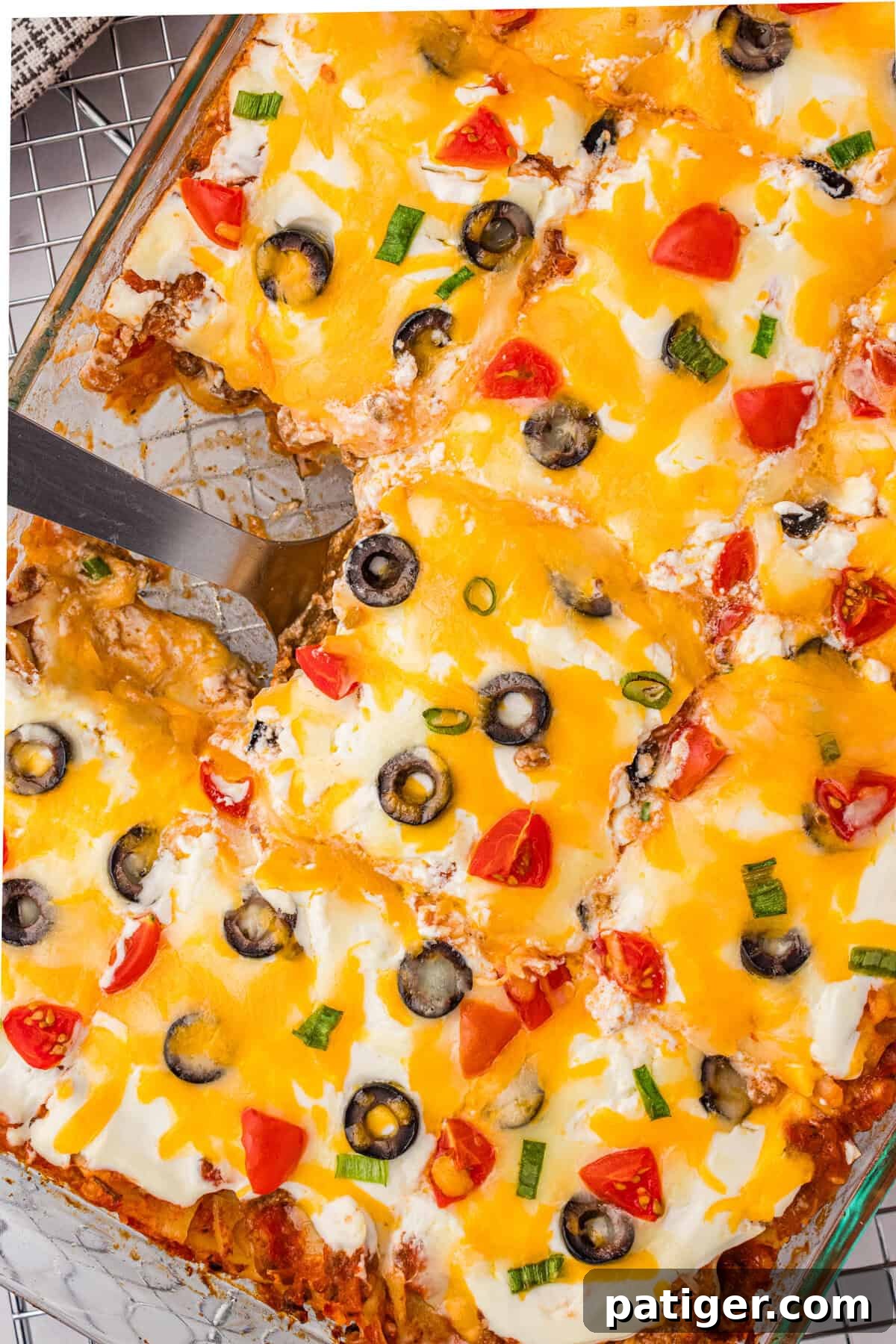 An inviting overhead shot of a neatly cut taco lasagna nestled in a baking dish, with a serving spatula poised to dish out a portion, showcasing its layered goodness.