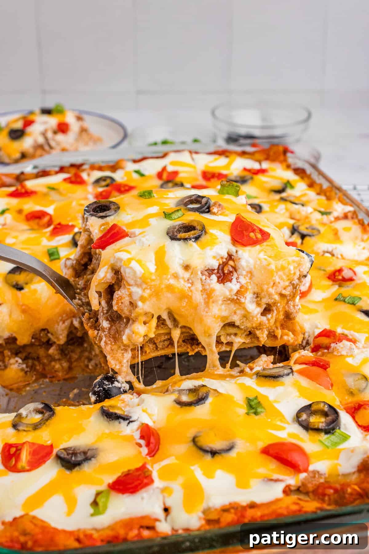 A glorious, cheesy slice of taco lasagna with lasagna noodles being expertly lifted from a glass baking dish, revealing its distinct, delicious layers.