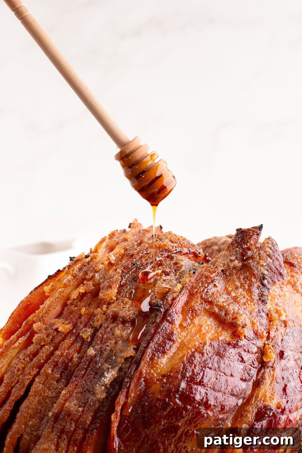 Golden Honey-Glazed Spiral Ham 3 A wooden honey dipper held above a spiral ham, with golden honey dripping onto the browned, sugary crust of the ham.