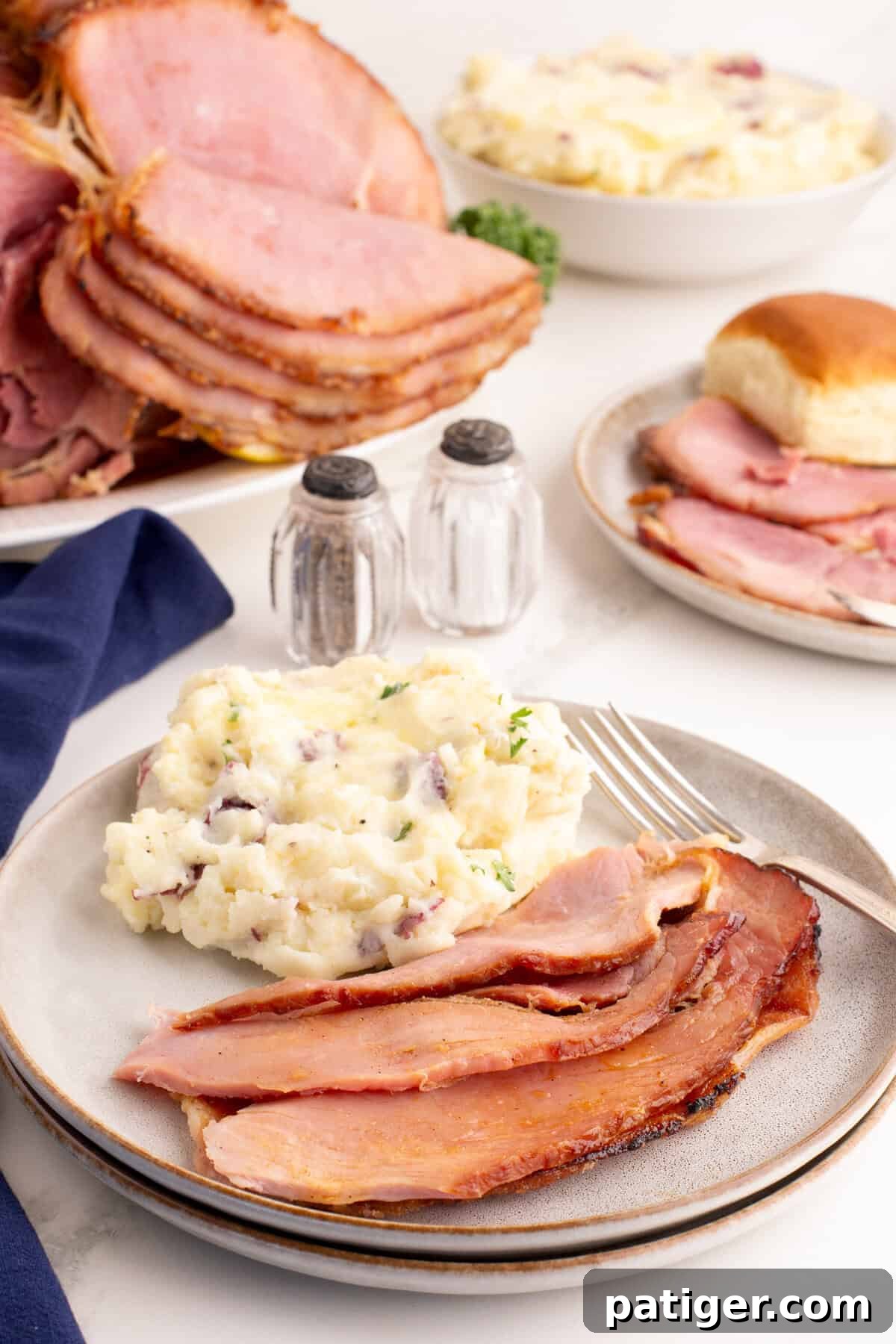 Golden Honey-Glazed Spiral Ham 8 Plate of spiral honey ham and mashed potatoes with more spiral cut honey baked ham and sides in the background.