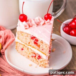 Close-up of a slice of cherry chip cake with pink frosting and cherries.