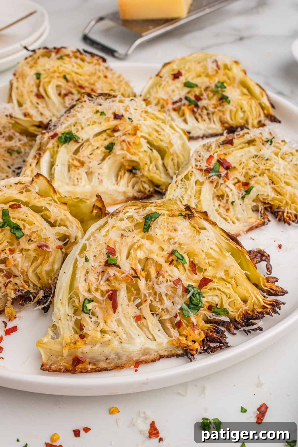 Caramelized Cabbage Bites 2 Tender-crisp roasted cabbage wedges adorned with golden garlic, melted Parmesan cheese, and a hint of red pepper flakes, artfully arranged on a pristine white plate.