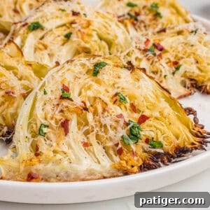 Caramelized Cabbage Bites 11 Close-up of roasted garlic parmesan cabbage wedges on a white plate, with golden brown edges, shredded parmesan, parsley, and red pepper flakes.