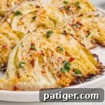 Caramelized Cabbage Bites 12 Close-up of roasted garlic parmesan cabbage wedges on a white plate, with golden brown edges, shredded parmesan, parsley, and red pepper flakes.