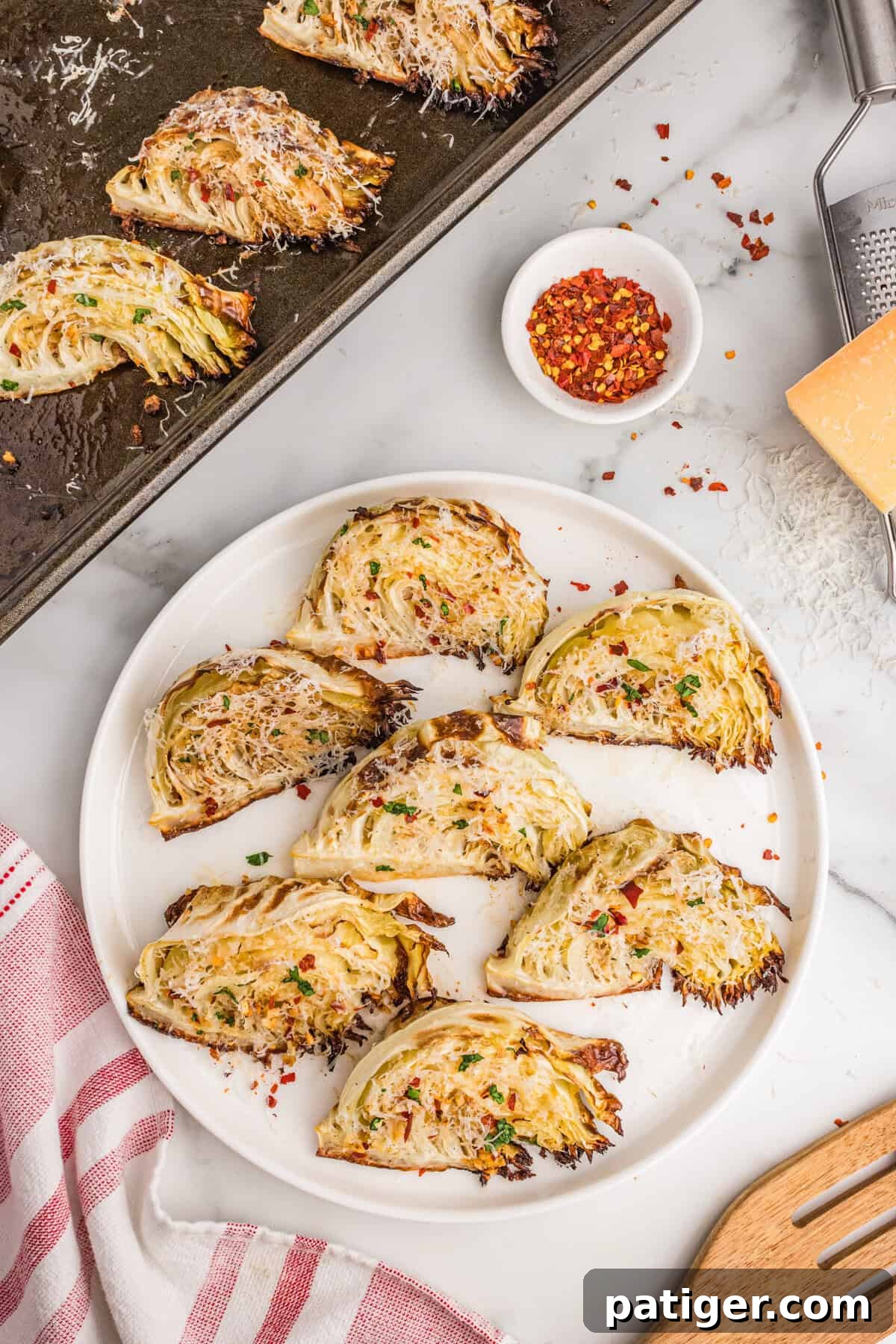 Caramelized Cabbage Bites 9 A stunning arrangement of roasted garlic parmesan cabbage wedges, meticulously placed on a pristine white serving plate and a practical baking sheet, garnished with a generous sprinkle of shredded parmesan, fresh parsley, and a hint of red pepper flakes for visual appeal and an extra touch of flavor.