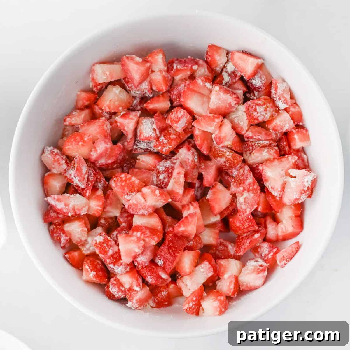 Scrumptious Strawberry Crumb Cake 3 A white bowl generously filled with vibrant, chopped fresh strawberries. The berries are lightly coated with a mixture of sugar and flour, indicating they are prepared and ready to be used as a luscious filling for the crumb cake, promising sweet and fruity goodness.