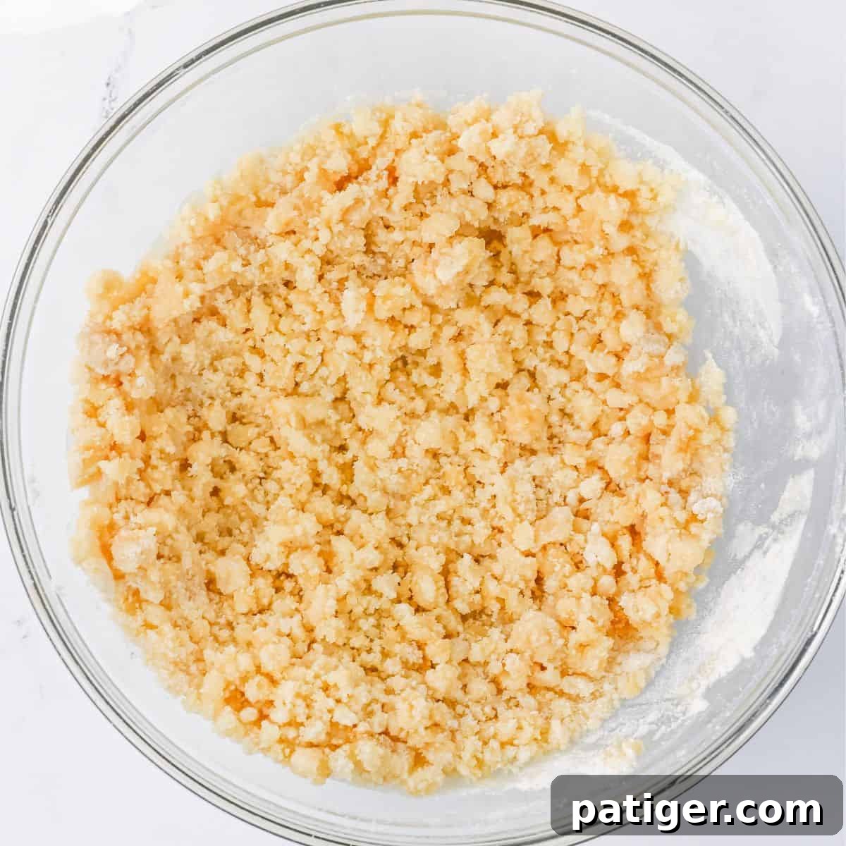 Scrumptious Strawberry Crumb Cake 4 A clear glass bowl showcasing a coarse, pale yellow crumb mixture. This mixture, consisting of flour, butter, and sugars, is perfectly textured for the crumb cake topping, appearing moist yet distinct in its individual crumbs.