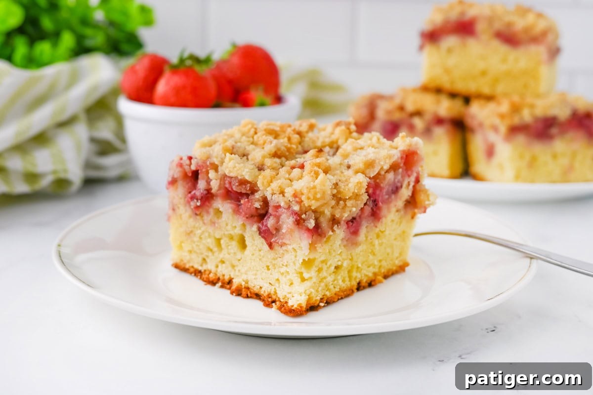 Scrumptious Strawberry Crumb Cake 8 A tempting slice of strawberry crumb cake artfully plated beside a small bowl brimming with fresh, ripe strawberries, highlighting the cake's rich fruit filling and inviting texture.