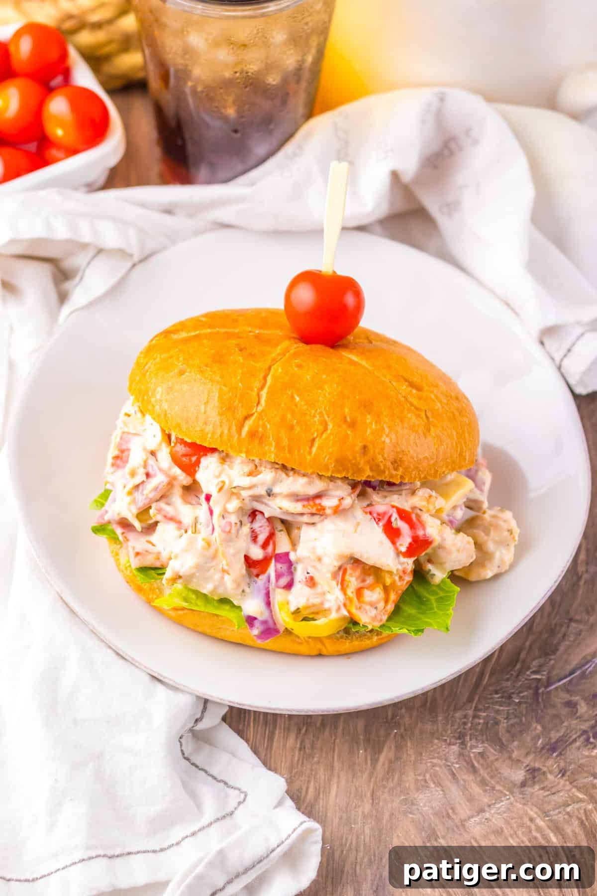 A hoagie chicken salad sandwich on a bun, topped with a cherry tomato on a toothpick.