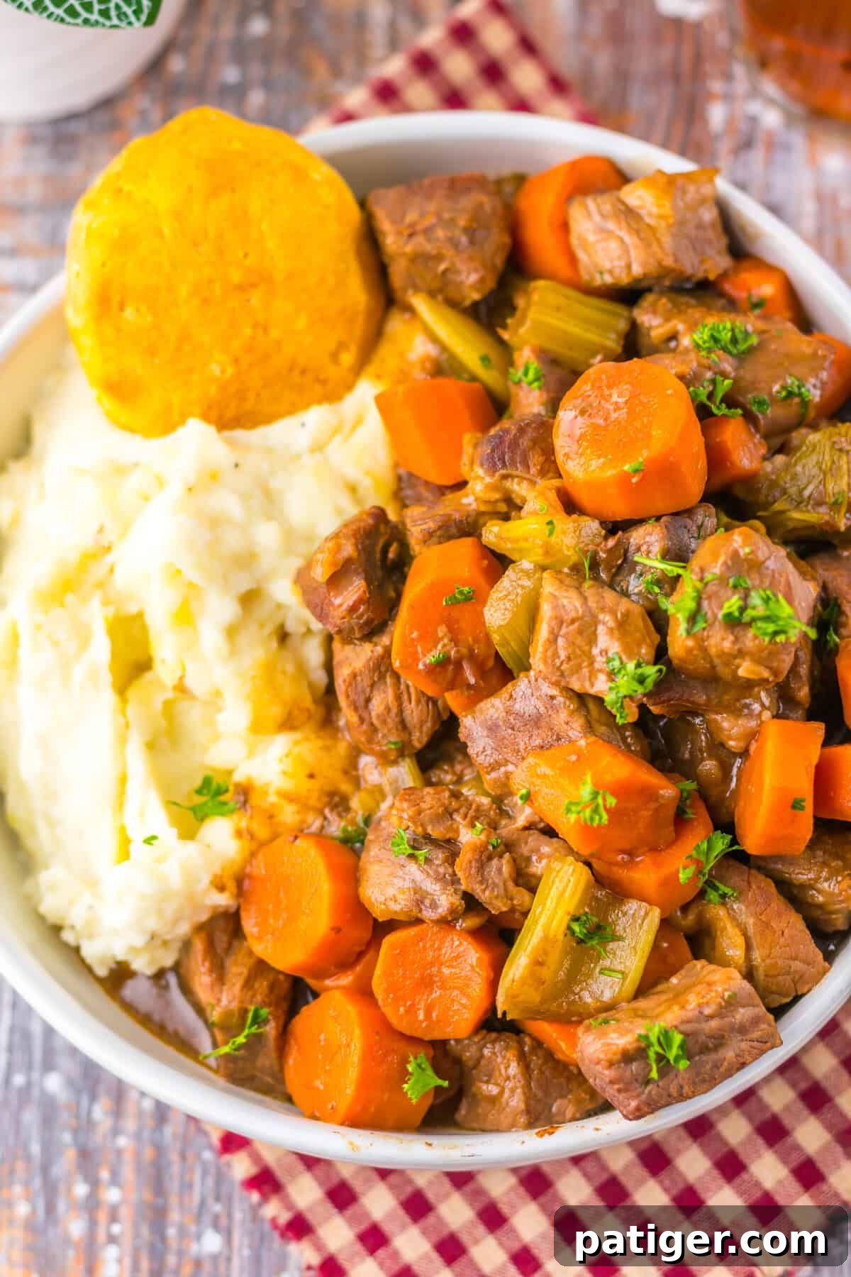 A bowl of hearty copycat Cracker Barrel pot roast with chunks of beef carrots, and celery in rich gravy. Creamy mashed potatoes and a golden biscuit are served on the side, creating a perfect comfort meal.