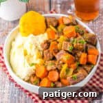 Bowl of crockpot cracker barrel copycat pot roast with carrots, celery, mashed potatoes, and a biscuit.
