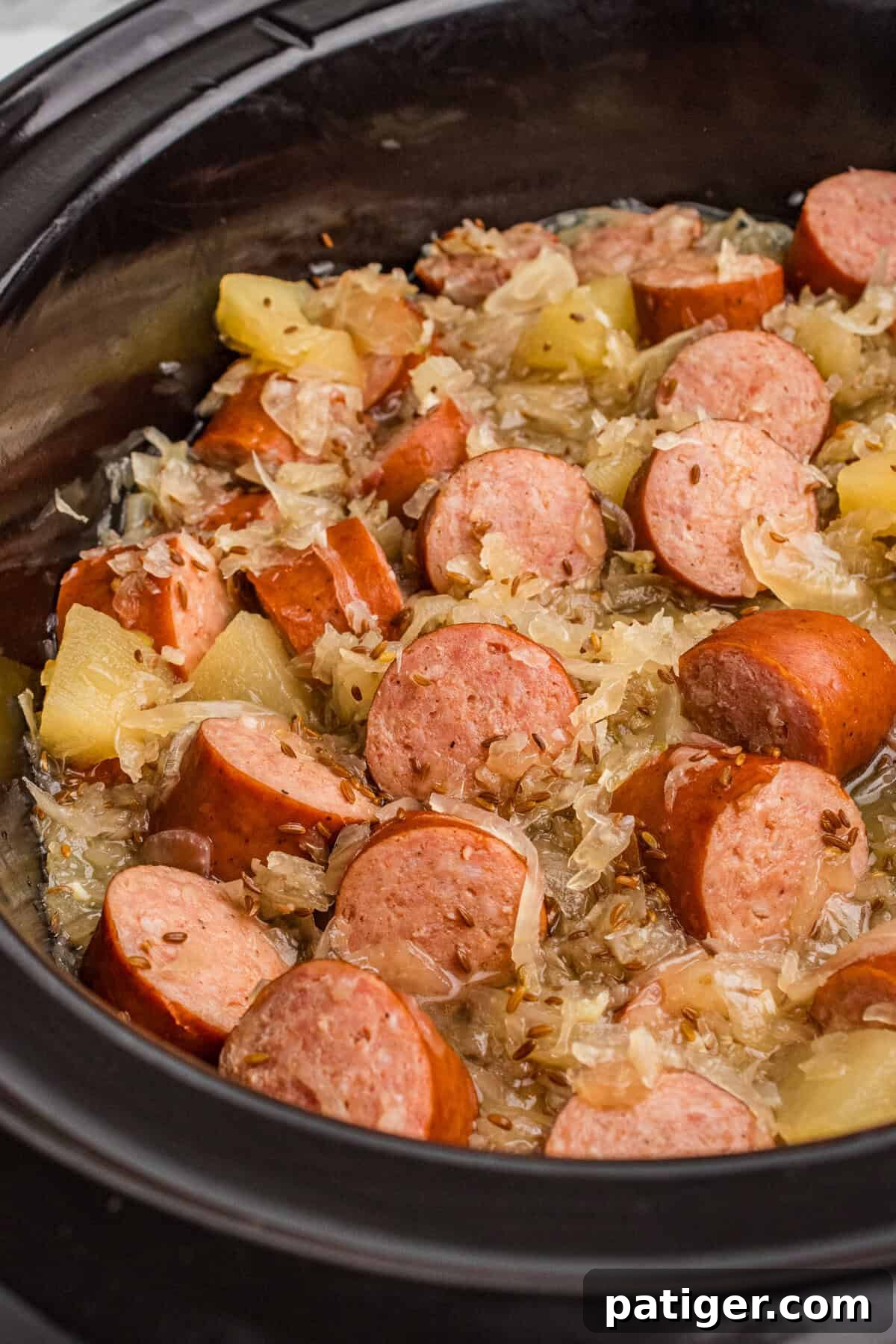 Kielbasa with sauerkraut, caraway seeds, and apple chunks in a crock pot.
