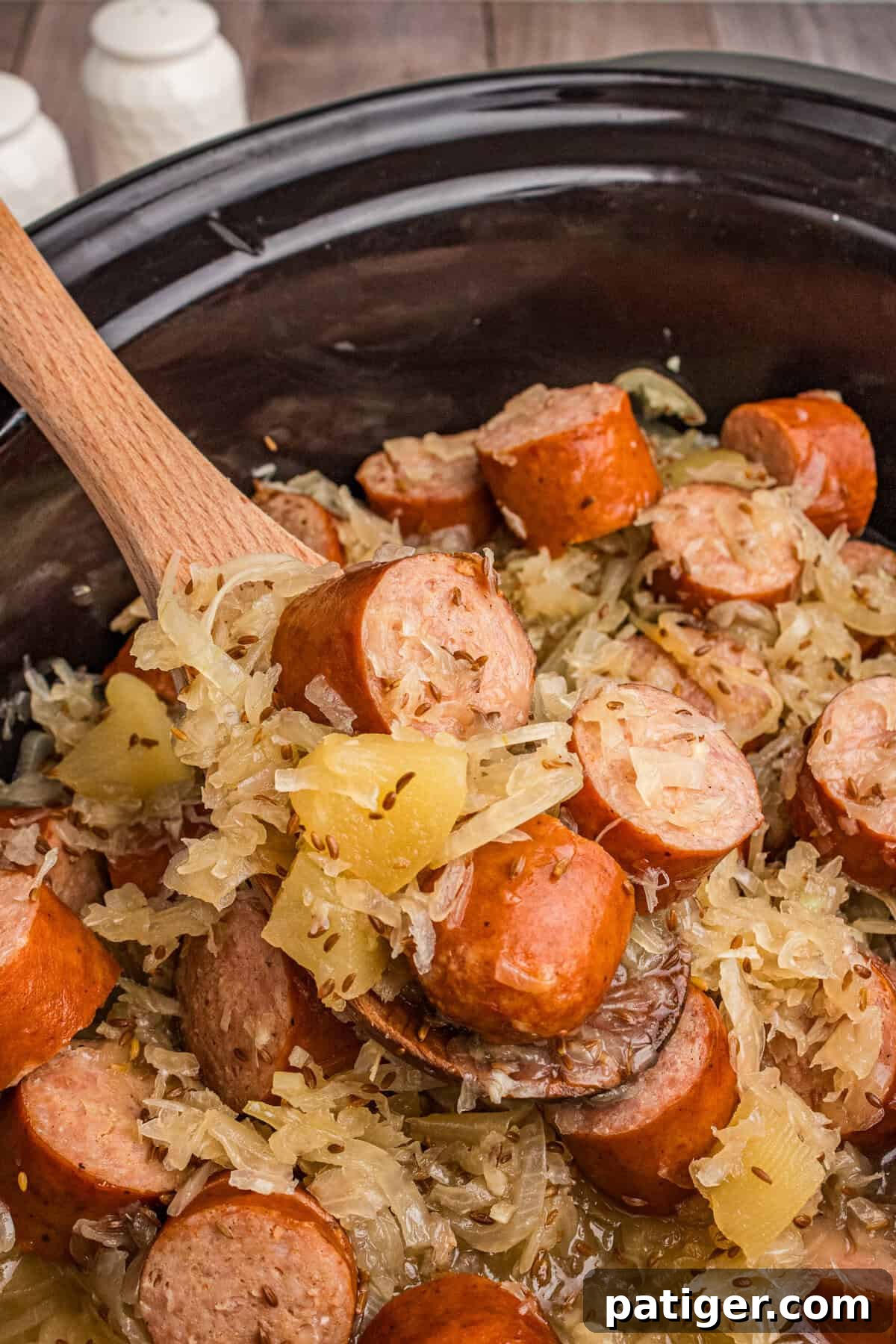 Spoon lifting kielbasa and sauerkraut from slow cooker.