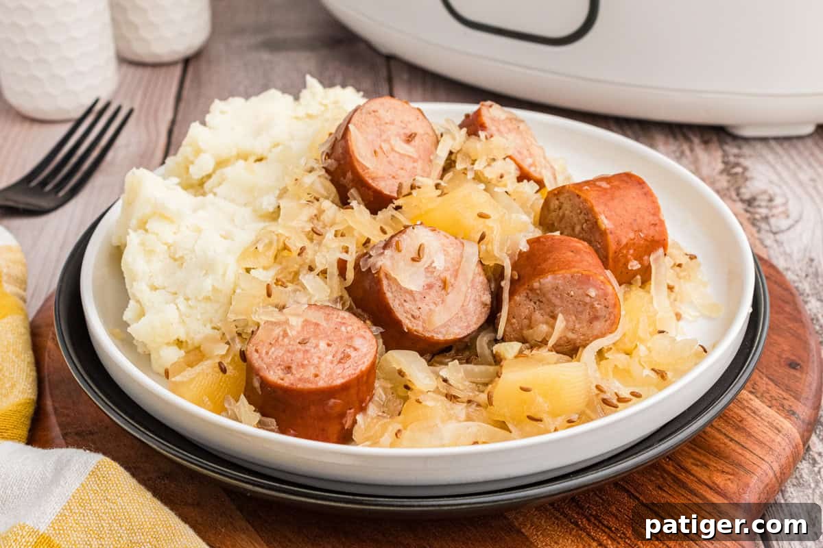 Sliced polish kielbasa and sauerkraut served with mashed potatoes. A slow cooker is n the background.