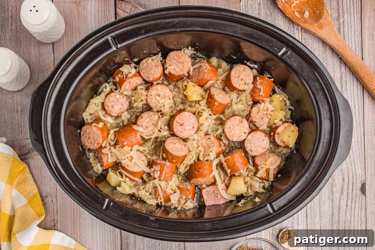 Sliced kielbasa with sauerkraut and apples in a slow cooker.