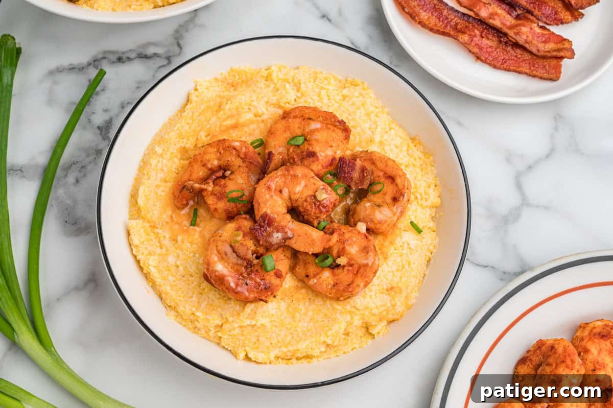 Loaded Cheesy Shrimp Grits 11 Bowl of cheesy grits topped with shrimp, bacon pieces, and scallions. The bowl is surrounded by fresh green onions and a plate of bacon.