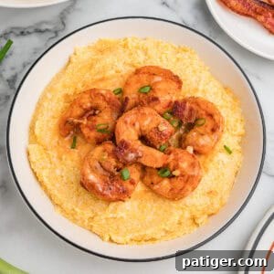 Loaded Cheesy Shrimp Grits 12 A bowl of cheesy shrimp and grits garnished with green onions and bacon.