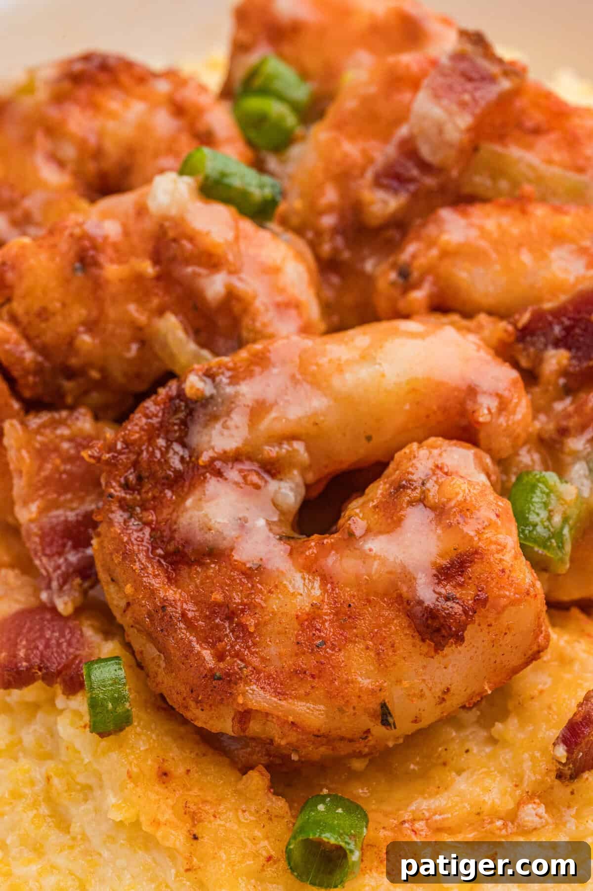 Loaded Cheesy Shrimp Grits 3 Saucy, seasoned shrimp resting on creamy yellow grits, with visible pieces of green onion and bacon.