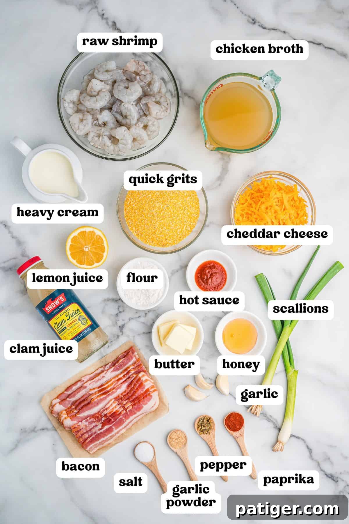 Loaded Cheesy Shrimp Grits 4 Overhead view of various labeled ingredients for cheesy shrimp and grits arranged on a marble surface. Items include raw shrimp, chicken broth, quick grits, cheddar cheese, heavy cream, lemon juice, flour, hot sauce, butter, honey, garlic, scallions, bacon, clam juice, and seasonings in wooden spoons: salt, garlic powder, pepper, and paprika.