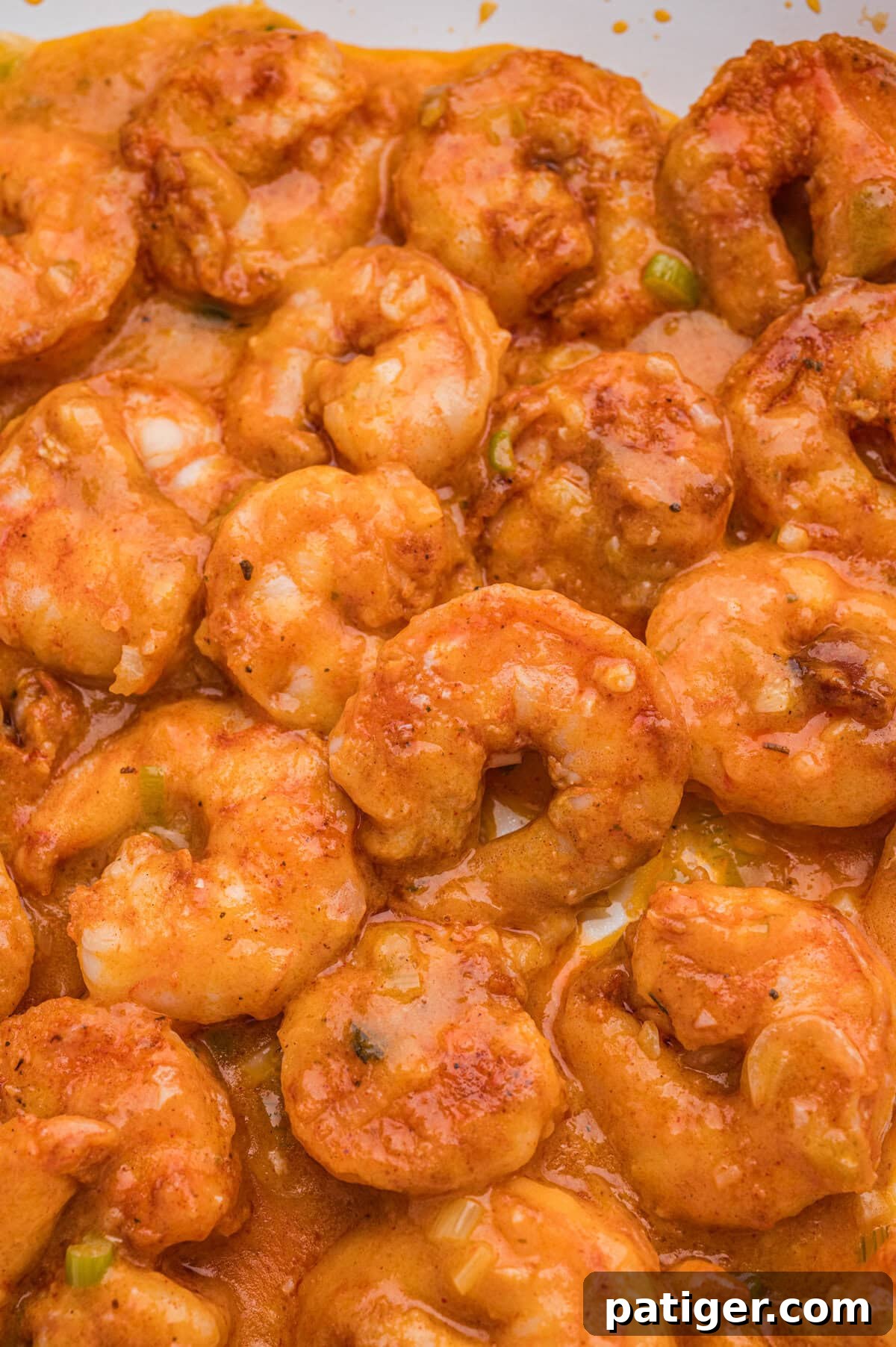 Loaded Cheesy Shrimp Grits 9 Close-up of cooked seasoned shrimp coated in a creamy orange sauce.