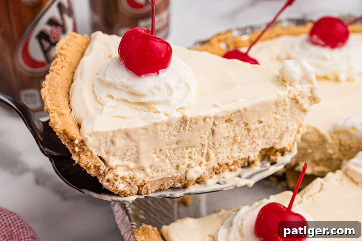 A slice of root beer float pie being lifted from the pan, showing creamy filling, graham cracker crust, and a topping of whipped cream and a cherry.