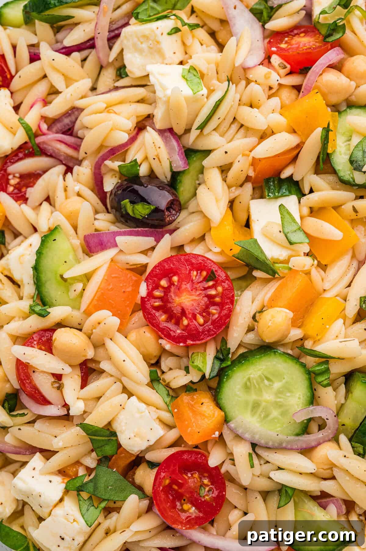 Extreme close-up of orzo salad showing detailed textures of vegetables and pasta.