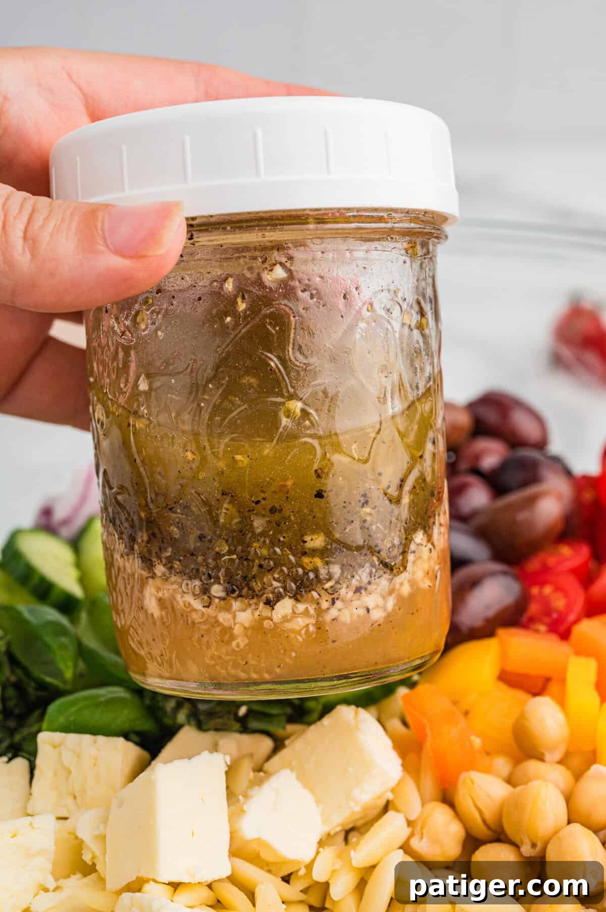 A jar of lemon vinaigrette dressing held above orzo salad.