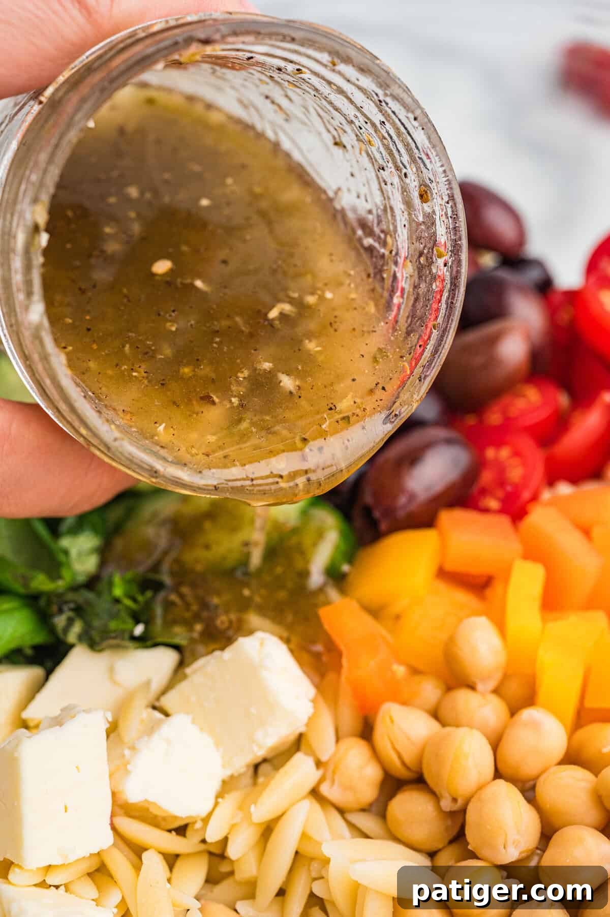 Salad dressing being poured from a jar over orzo salad ingredients.