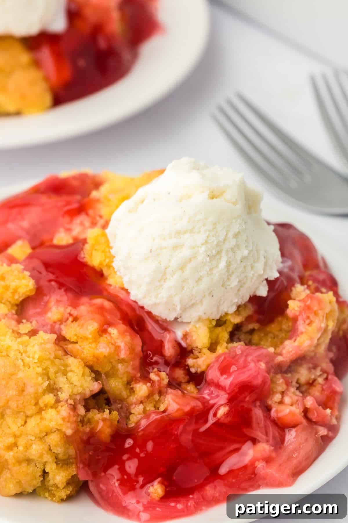 A slice of golden rhubarb dump cake on a white plate, topped with a generous scoop of melting vanilla ice cream. The vibrant red rhubarb filling peeks out from under the crumbly, baked cake topping.