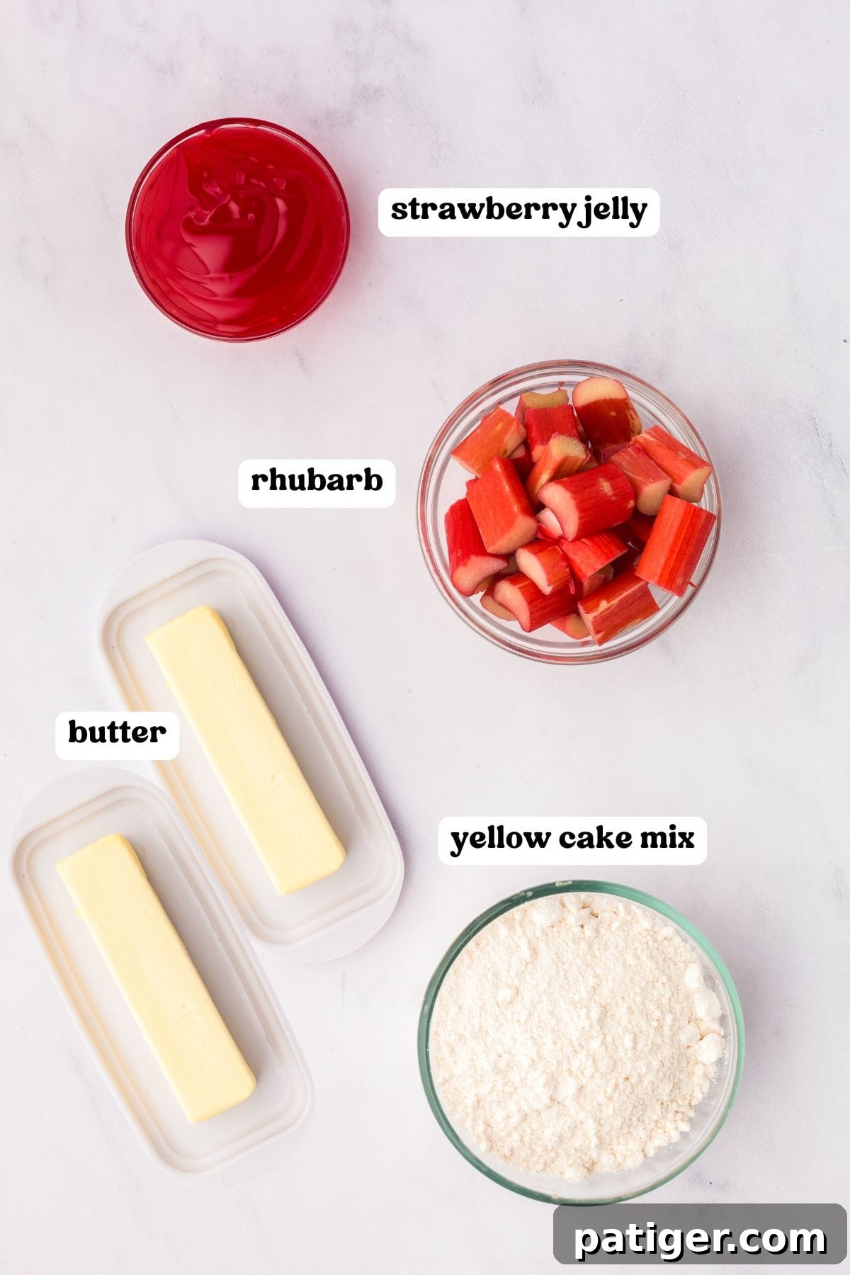 An overhead view of four carefully arranged and labeled ingredients: a jar of vibrant red strawberry jelly, freshly chopped green and red rhubarb stalks, two sticks of cold butter, and a box of yellow cake mix.