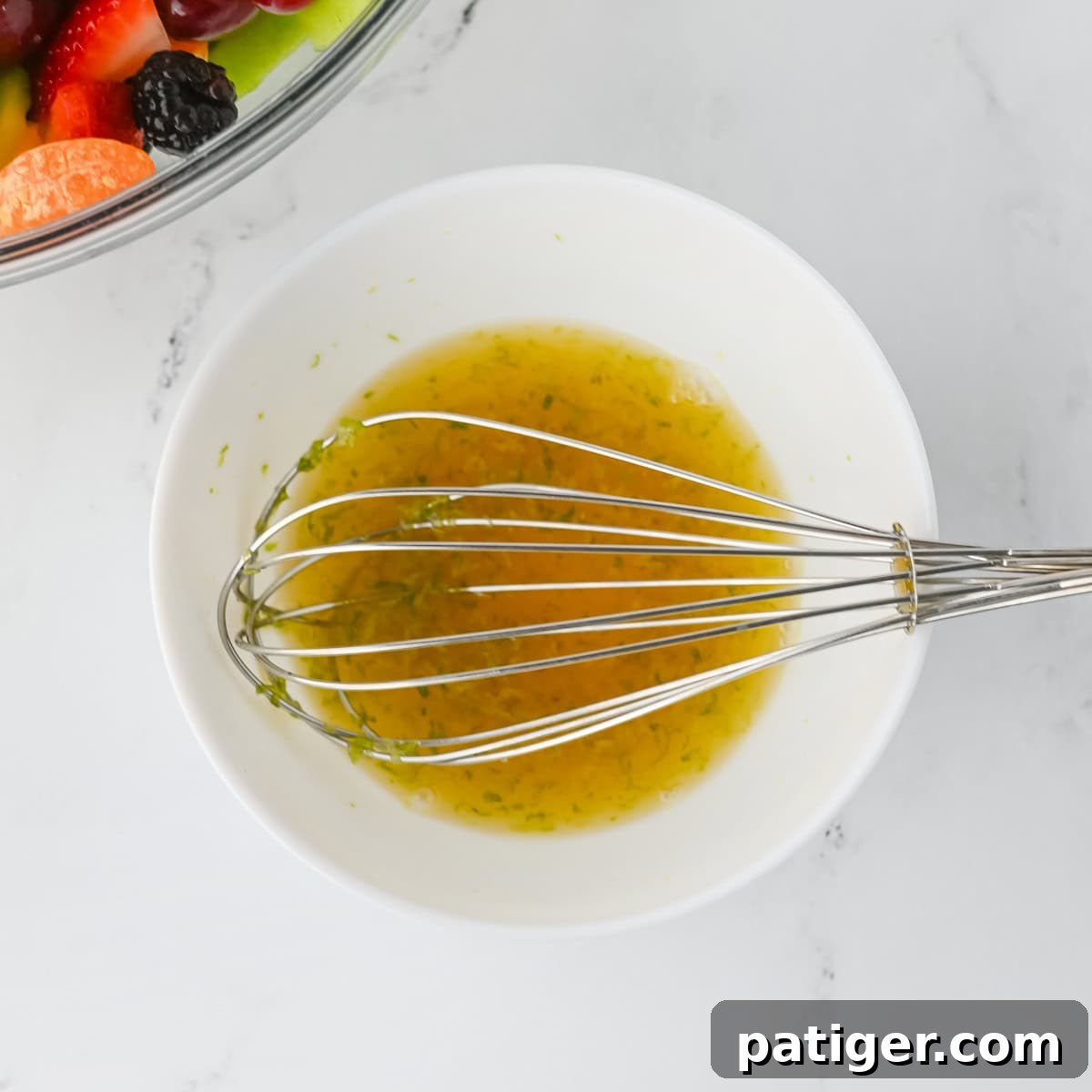 A small glass bowl containing the golden honey lime dressing, with a whisk resting in it. The liquid appears smooth and well-combined, ready for use.