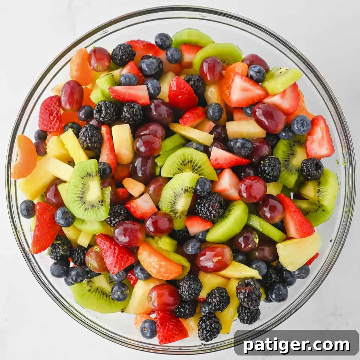 A large clear glass bowl filled with a vibrant rainbow fruit salad, showcasing the variety of fresh fruits after being tossed with the dressing. The colors are bright and appealing.