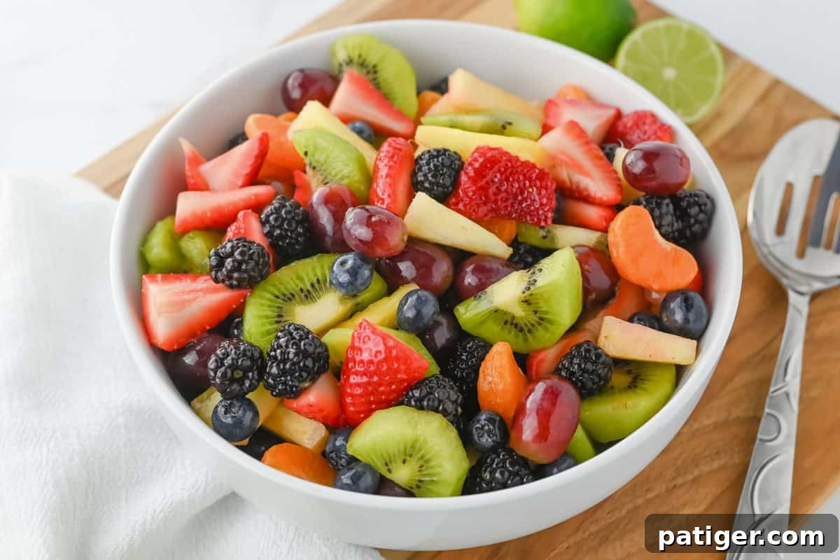 Side view of a bountiful fruit salad in a white ceramic bowl, showcasing the layered textures and vibrant colors of the fresh fruits, all glistening with the honey lime dressing.