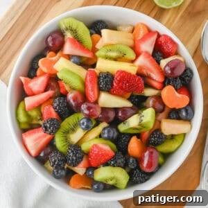 Fruit salad with honey lime dressing in a white bowl with sliced strawberries, kiwi, pineapple, grapes, blackberries, blueberries, and clementine slices.