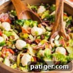 Chopped antipasto salad with mozzarella, meats, lettuce, and vegetables, in a wooden bowl with wooden serving utensils.