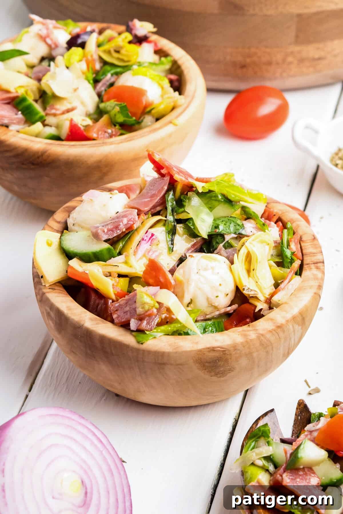 Two small wooden bowls filled with Italian antipasto salad including mozzarella, meats, lettuce, and vegetables.