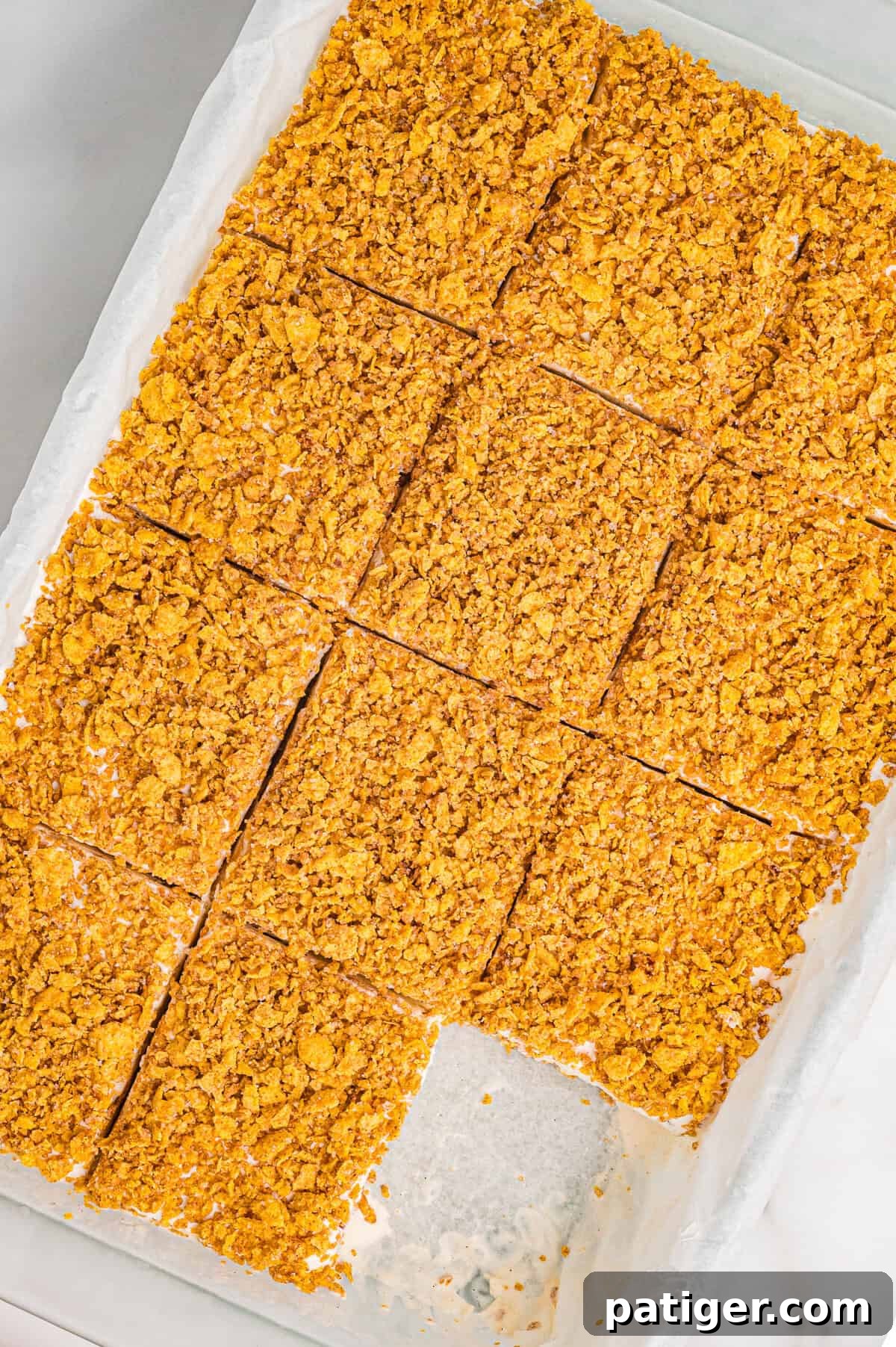 Golden Fried Ice Cream 8 Overhead view of a parchment-lined pan filled with fried ice cream dessert cut into even square portions. Each square has a crunchy golden cornflake topping, and one bar has been removed, revealing the creamy interior and base layer.