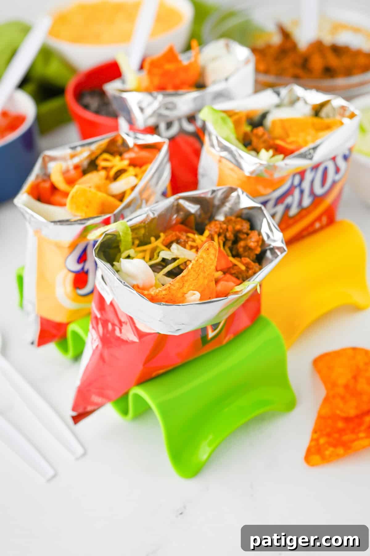 An appetizing close-up of multiple walking tacos served in their original Fritos and Doritos bags. Each bag is generously filled with perfectly seasoned ground beef, a sprinkle of shredded cheese, freshly chopped tomatoes, crisp lettuce, black beans, and a dollop of creamy sour cream.