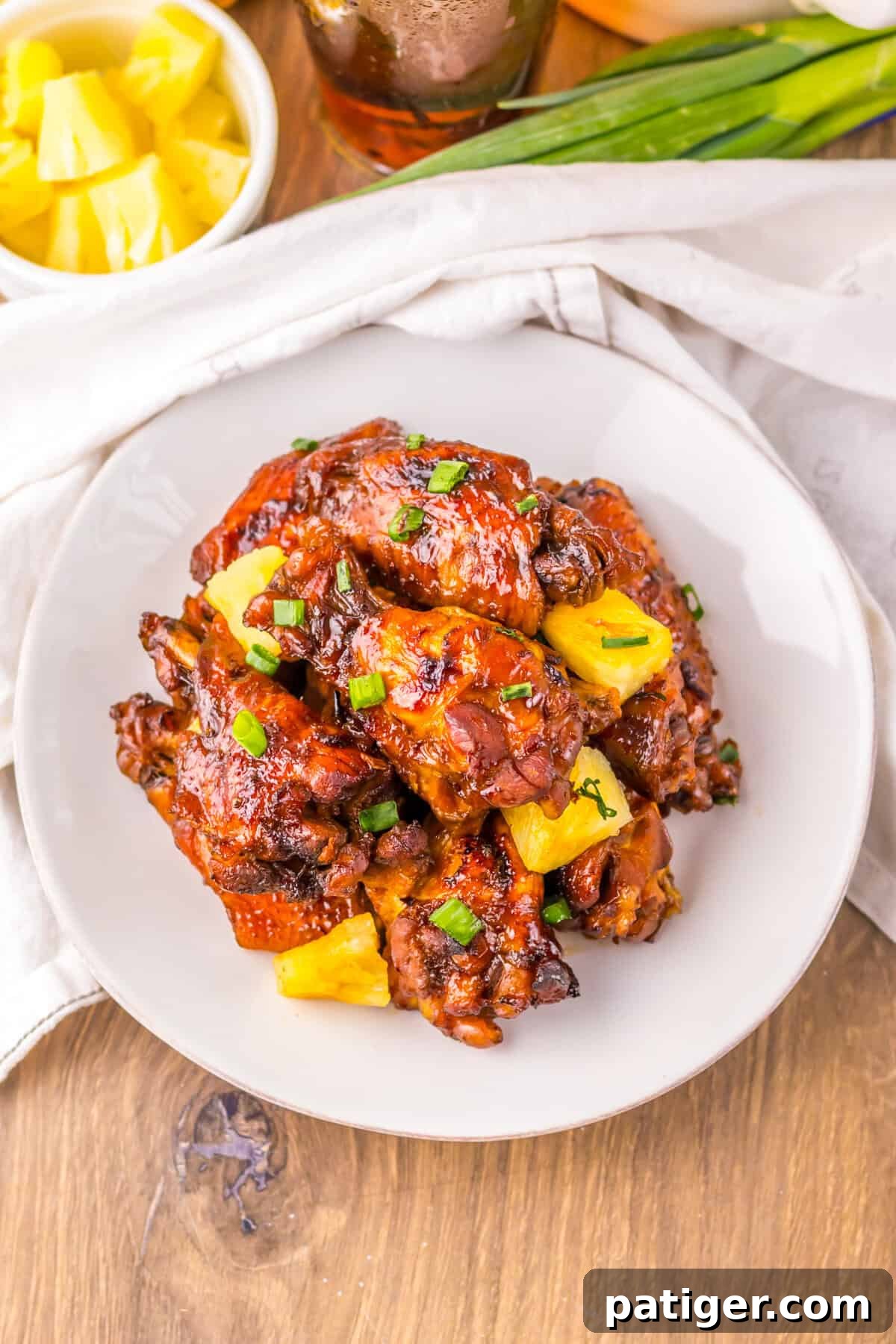 Overhead photo of a plate filled with slow cooker Hawaiian pineapple chicken wings garnished with vibrant pineapple chunks and fresh green scallions. The wings are perfectly glazed and ready to be enjoyed.