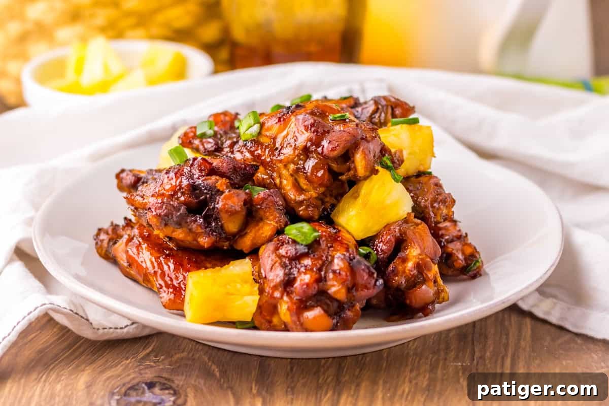 Hawaiian chicken wings on a white plate, featuring a glossy, dark glaze and garnished with pineapple chunks and chopped scallions, showcasing their appetizing appeal.